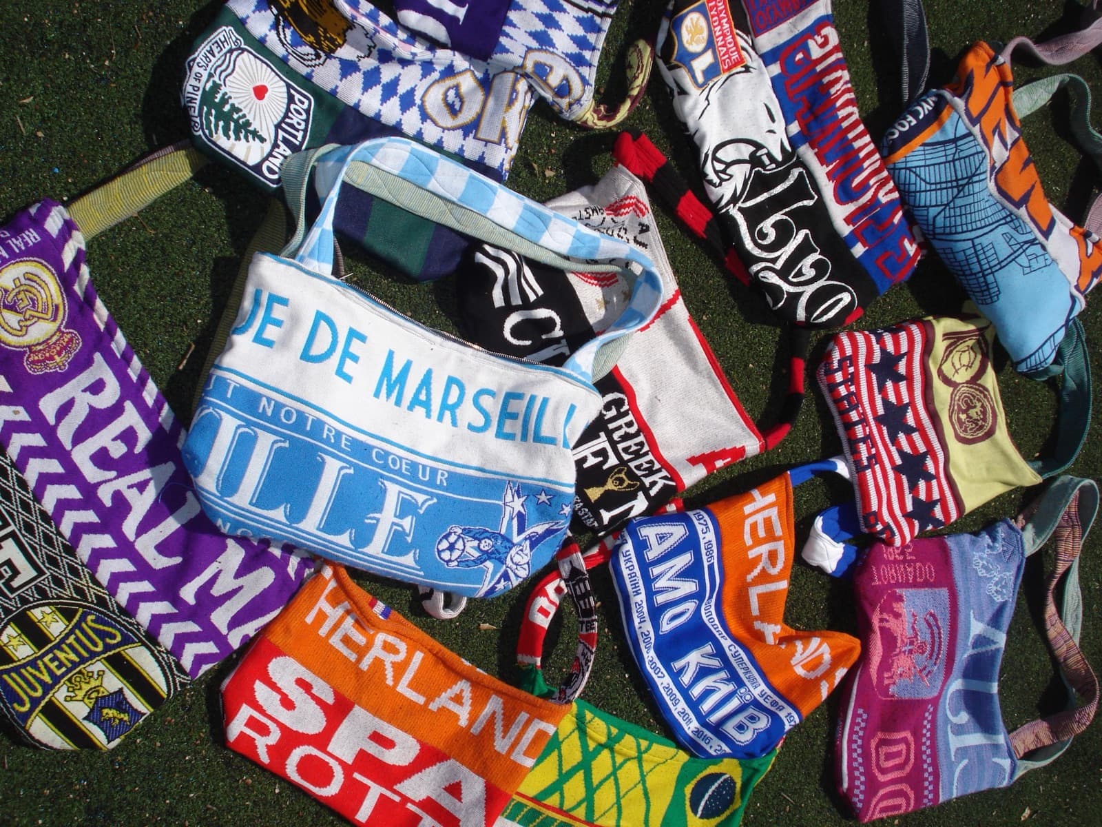 A pile of one-of-a-kind bags made from football scarves — Marseille, Real Madrid, Lyon, Dynamo Kyiv and more